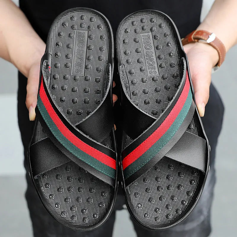 Men's cowhide leather beach flip-flops with non-slip sole in black, on a sandy background.
