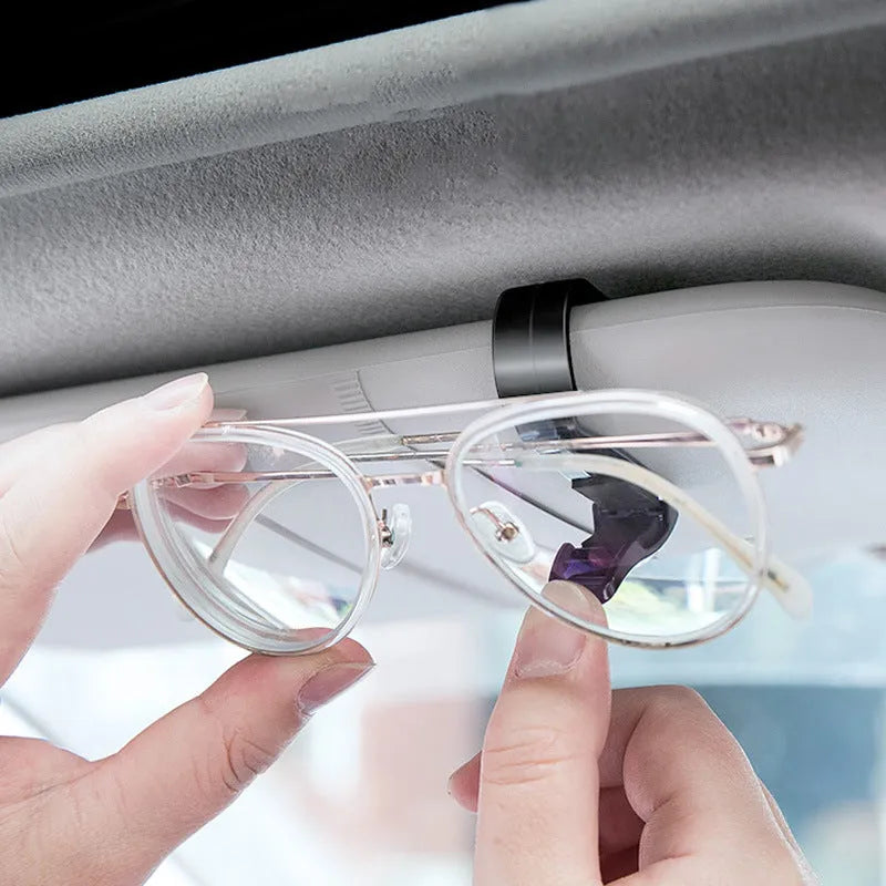 Black plastic car sun visor clip holding a pair of sunglasses and a parking ticket.