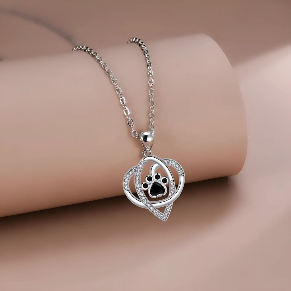 Close-up of a copper pendant necklace showing a charm with dog paw and cat footprint designs on a cross chain.