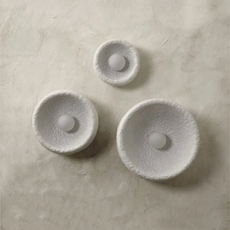 Japanese modern simple wall lamp with white resin shade in three size options on a plain wall.