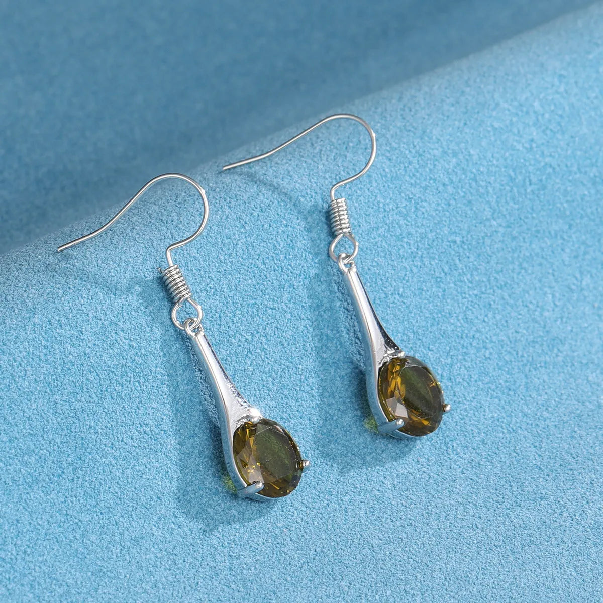 Olive green topaz coloured drop-shaped retro earrings for women on a plain background.
