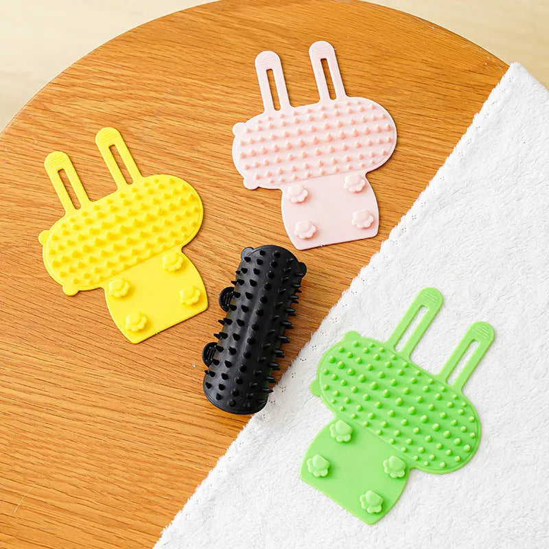 Silicone cat grooming comb with adjustable strap mounted on table leg, showing rounded teeth for pet hair removal