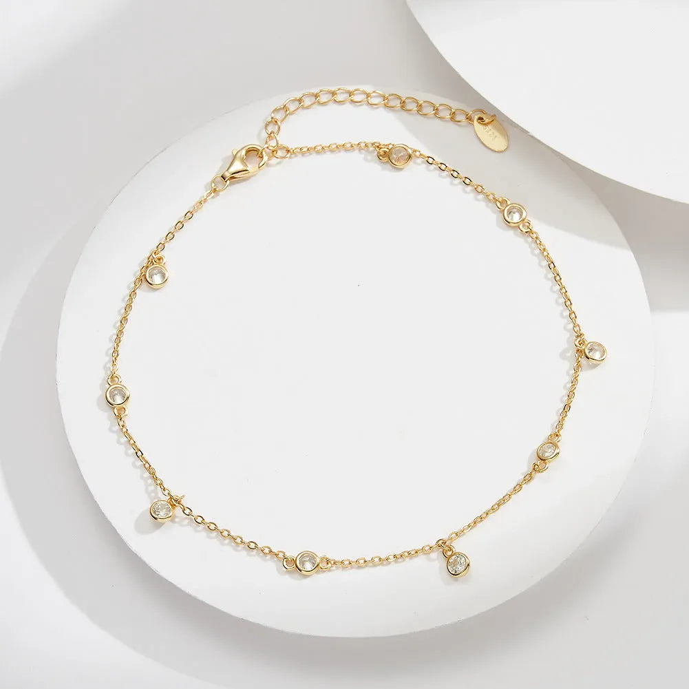 Women's silver geometric zirconium pendant anklet on an ankle, shown in gold and platinum colour options.
