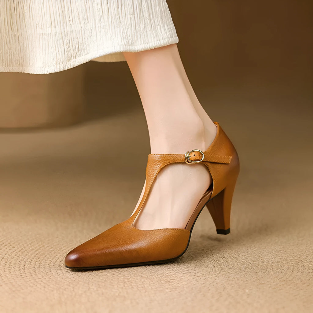 Brown retro women's T-strap sandals with a closed toe, low upper, and a stout high heel on a wooden floor.