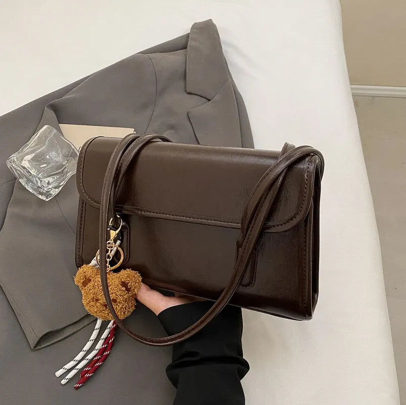 Brown women's PU leather crossbody shoulder bag with pendant, showing front view and adjustable double straps.
