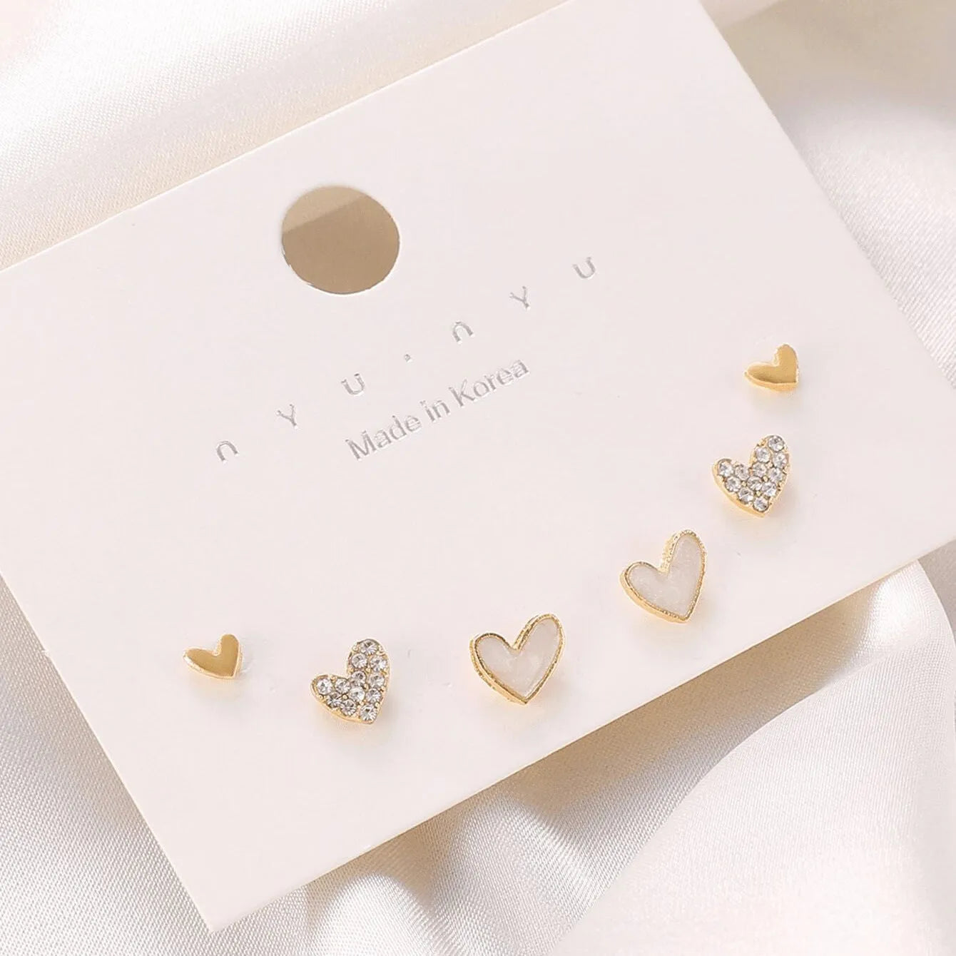 Three pairs of heart-shaped girly earrings in gold, black, black and white, and pink colours
