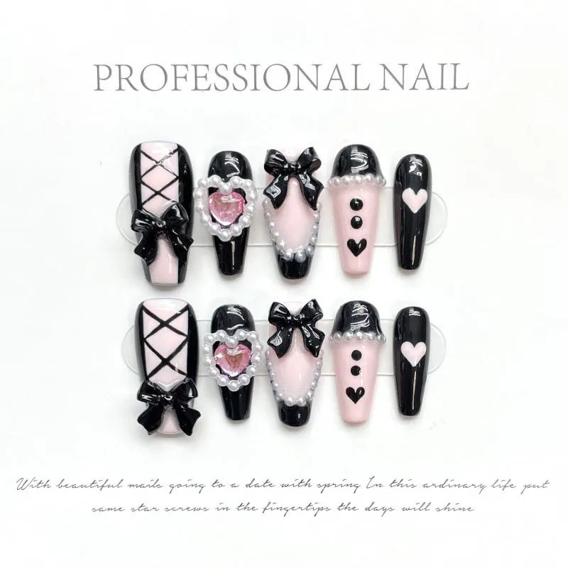 Hand-painted black false nails with pink peach hearts, XINGX text, bows, and a cat's eye shimmer effect.