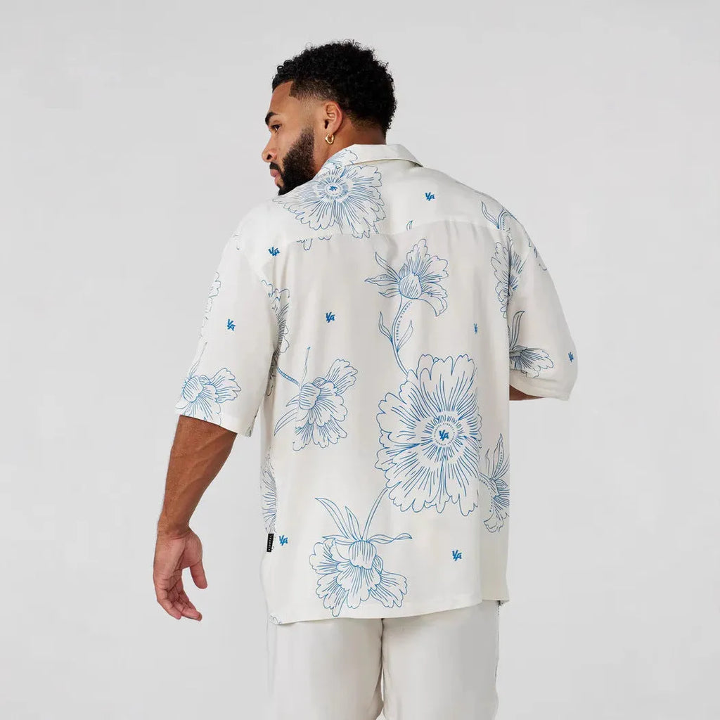 A man's loose-fitting, short-sleeve casual top with a floral print, shown in a neutral colour.