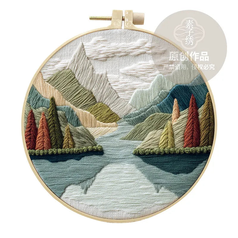 Landscape embroidery DIY kit with cotton fabric, printed pattern, embroidery frame, needles, and thread on wooden surface