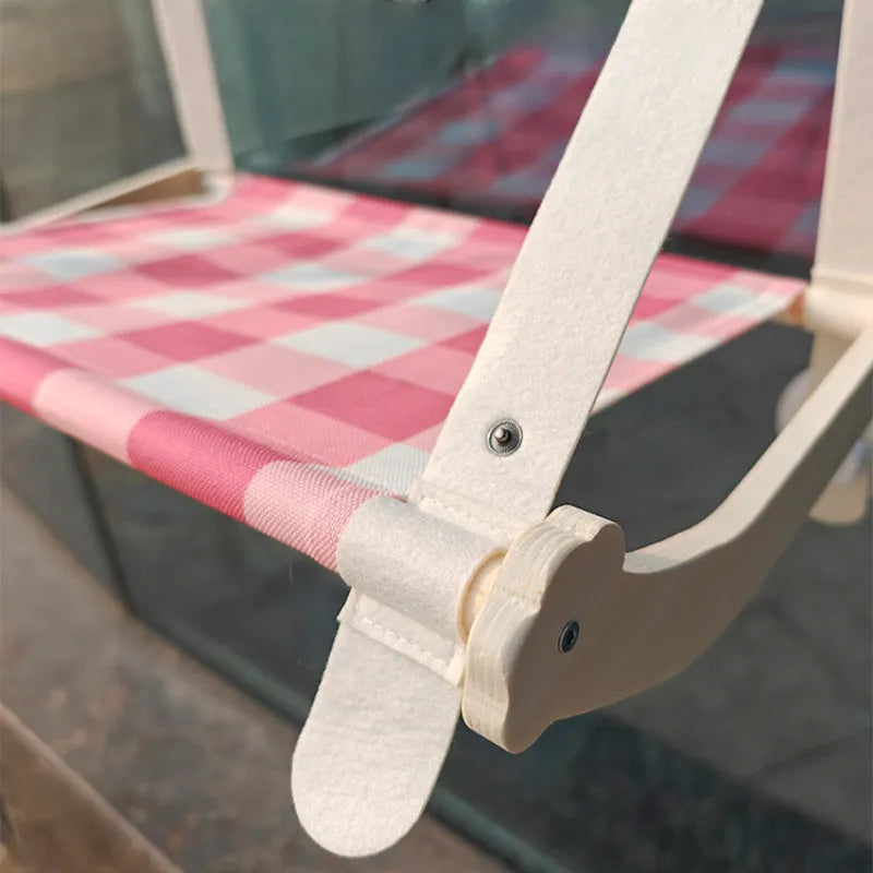 Foldable wooden cat window hammock with suction cups attached to a glass pane.
