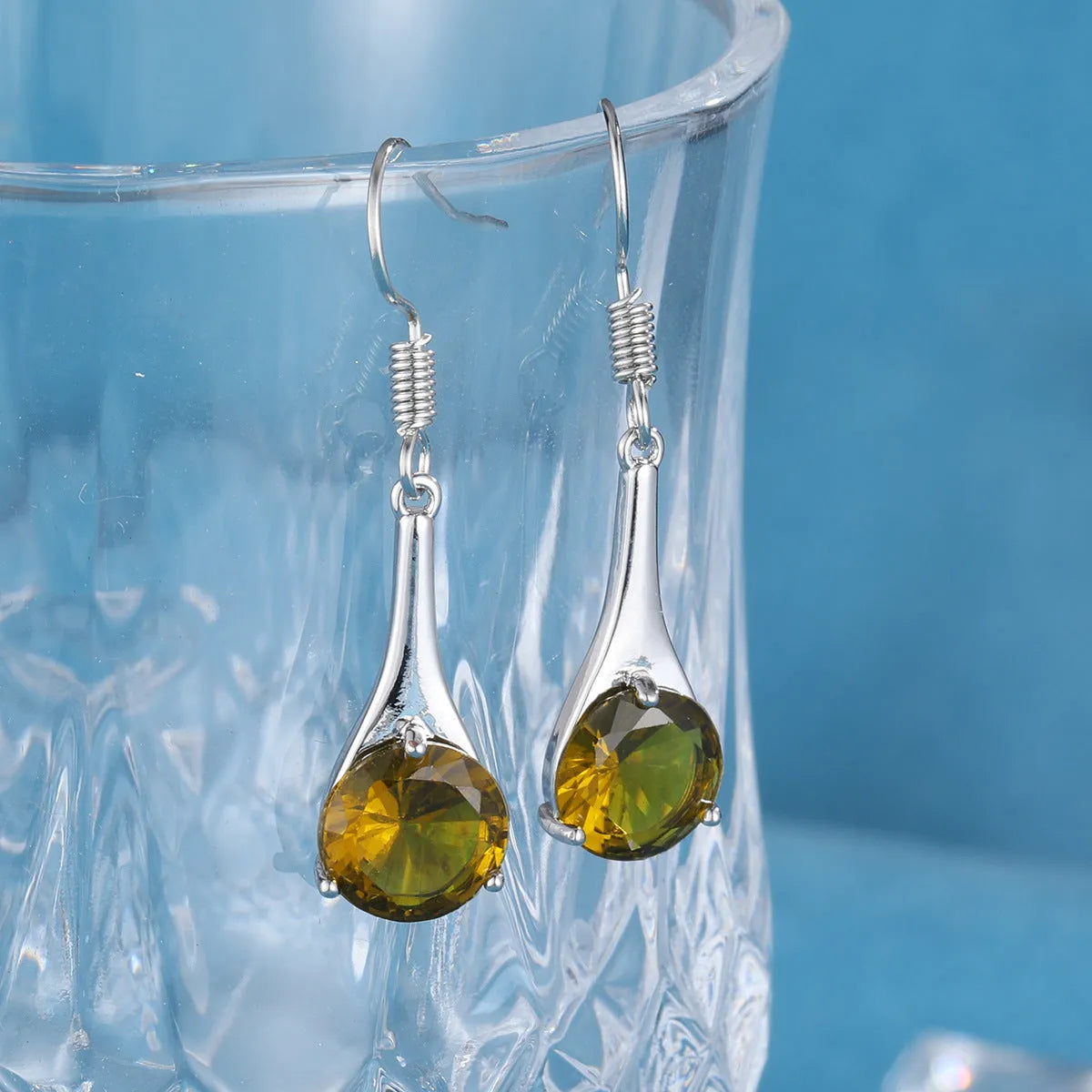 Olive green topaz coloured drop-shaped retro earrings for women on a plain background.