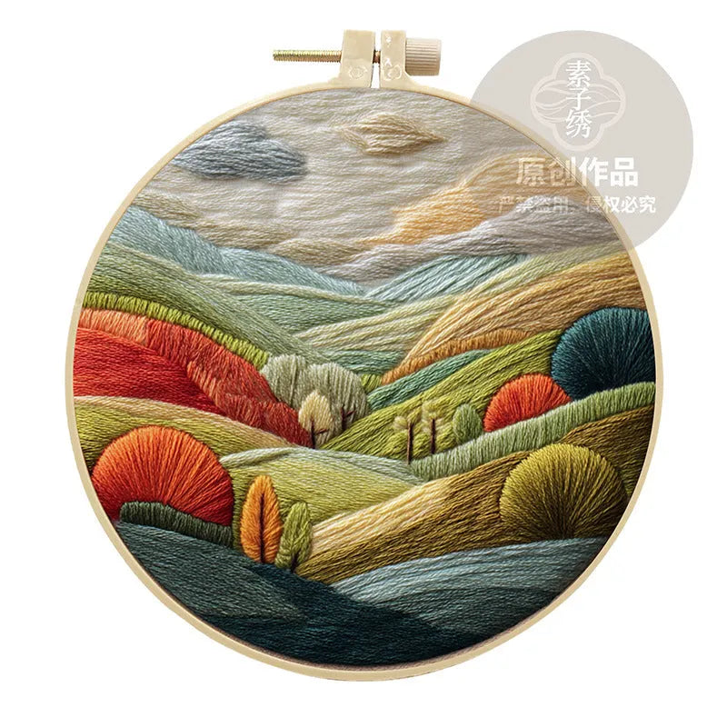 Landscape embroidery DIY kit with cotton fabric, printed pattern, embroidery frame, needles, and thread on wooden surface