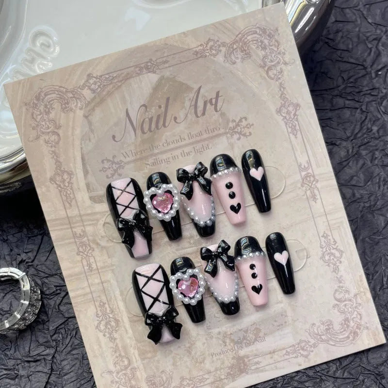 Hand-painted black false nails with pink peach hearts, XINGX text, bows, and a cat's eye shimmer effect.